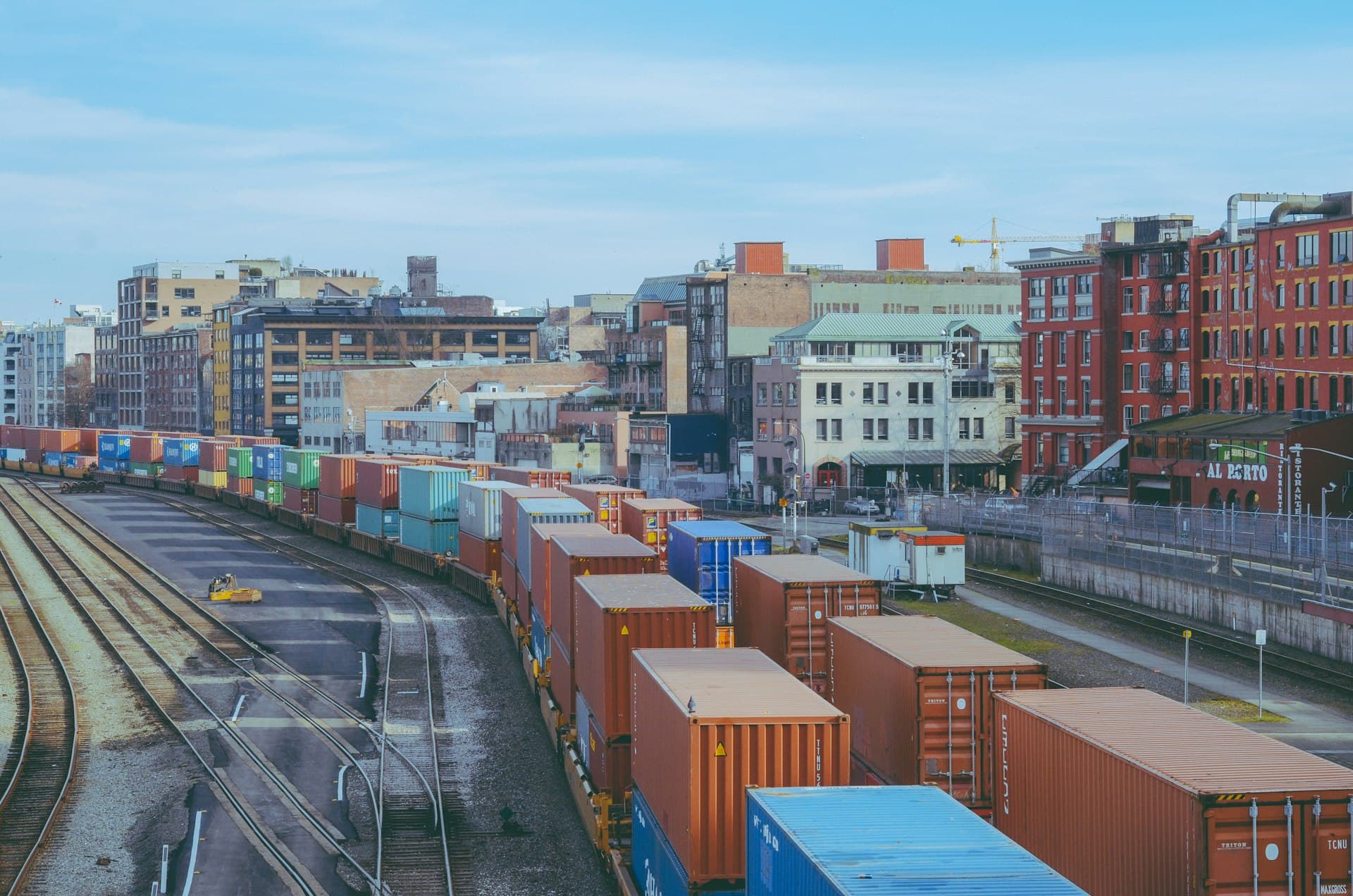 Intermodal freight train loaded with colorful shipping containers winding through an urban rail corridor