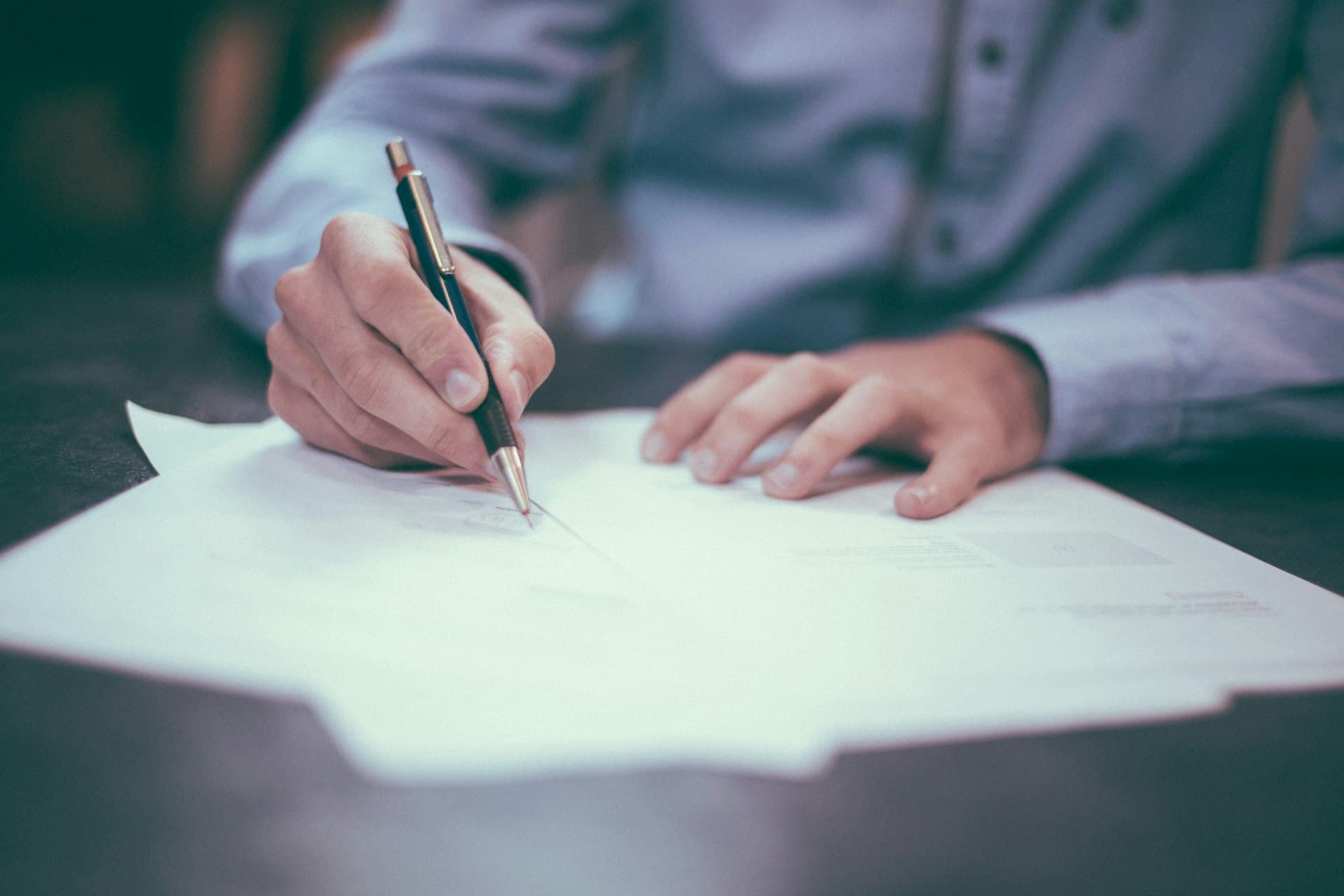 Close-up of hands in a blue shirt signing shipping documents with a pen at a desk