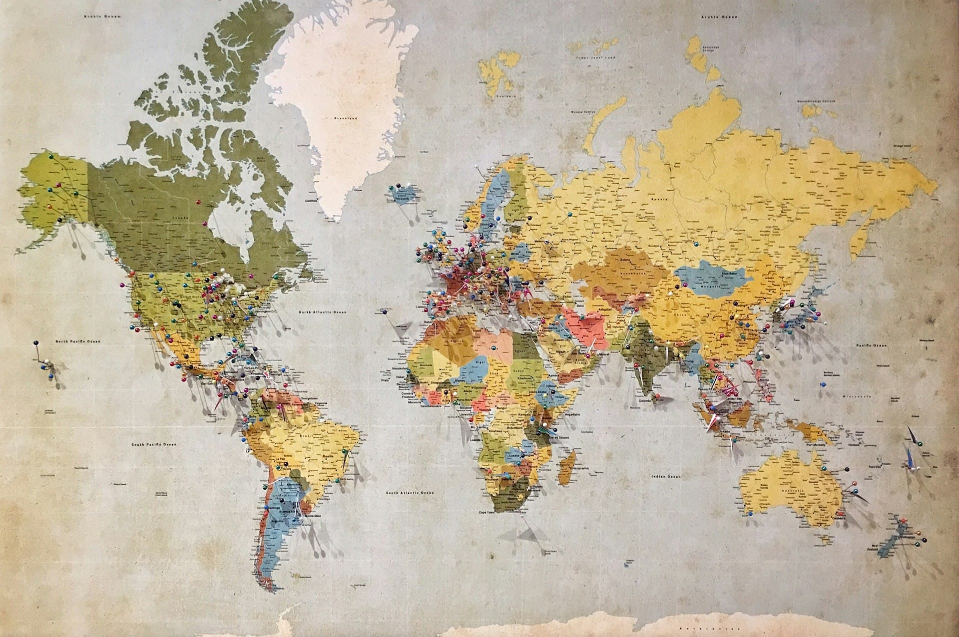 World map in muted blue, green, and yellow tones covered with location pins marking global destinations
